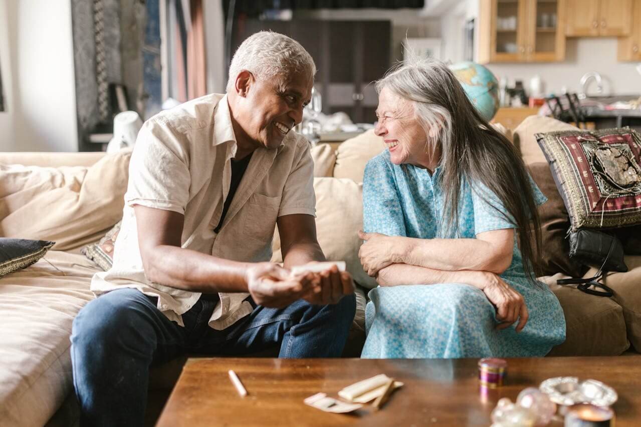 Happy elderly couple sitting together on their couch, smiling while looking at a laptop